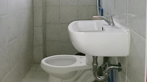A small, tiled bathroom with a toilet, a sink, and a window.