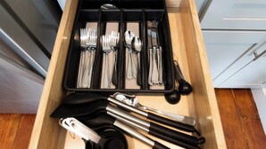 A drawer containing various kitchen utensils including forks, spoons, knives, and tongs. - The Edison (Lewiston)
