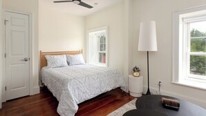 A bedroom with a bed, a ceiling fan, a lamp, a clock, and a window. - The Edison (Lewiston)