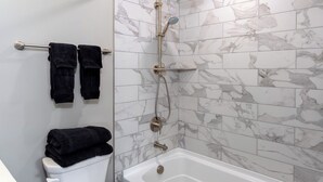 A bathroom with a shower, toilet, and a towel rack with two towels. - The Edison (Lewiston)