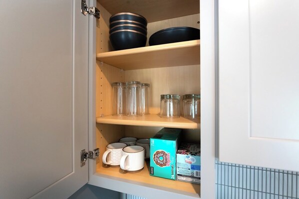 A kitchen cabinet with shelves containing kitchenware, including bowls, jars, and a box of coffee. - The Edison (Lewiston)