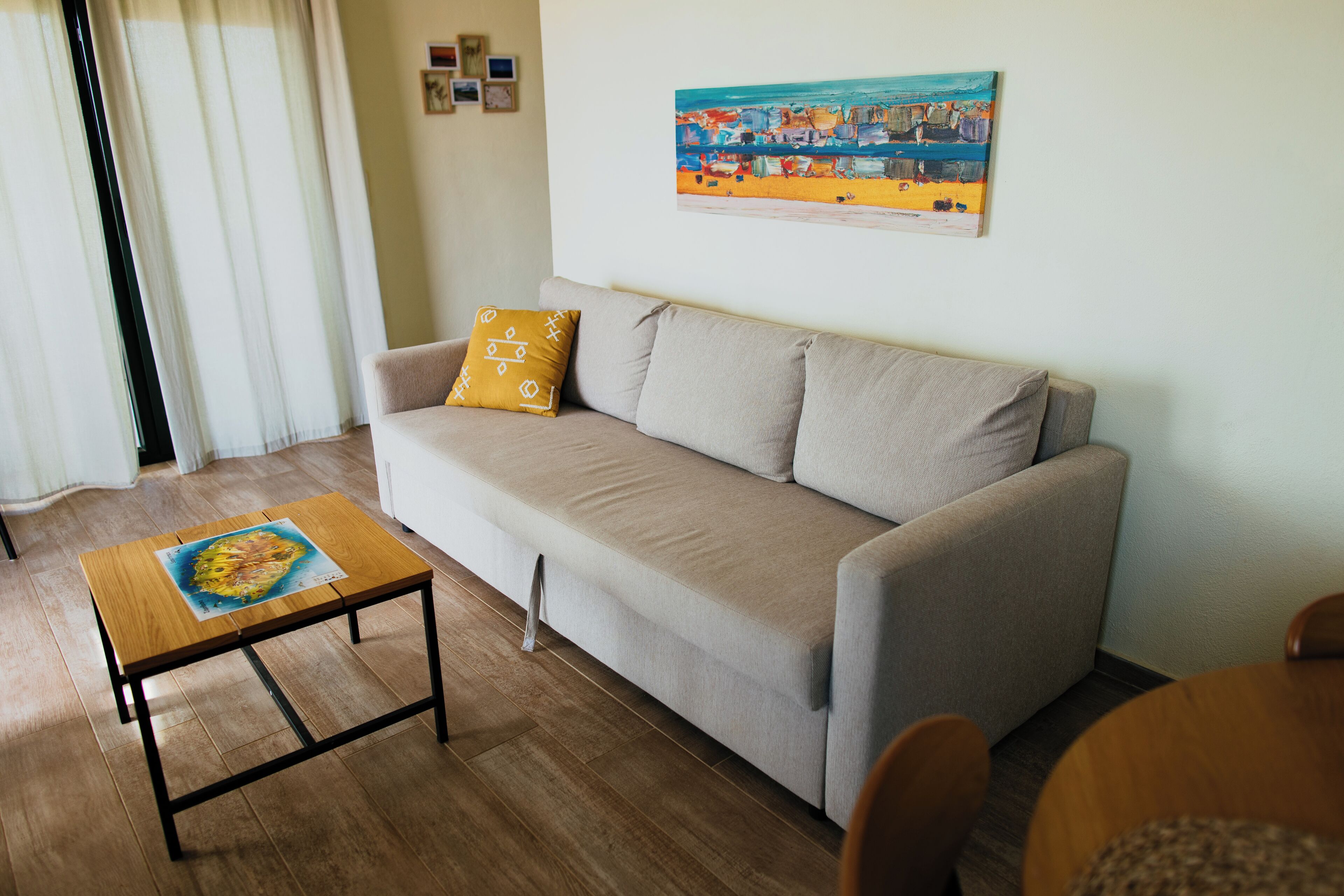 Un salón con un sofá color beige, una mesa de centro de madera con un cuadro, y un cuadro en la pared.