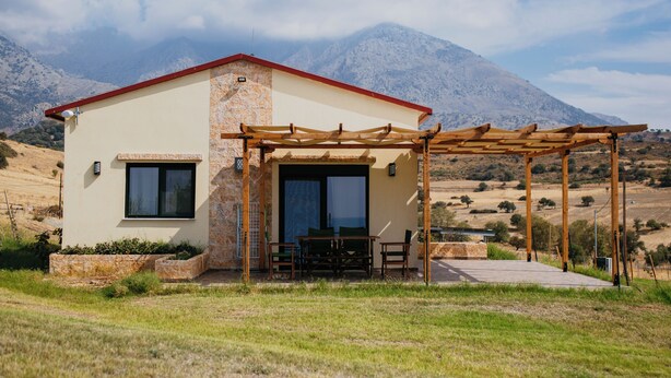 A modern house with a patio, a dining area, and a mountain backdrop. - Pezoulia Cottages (Samothrace)