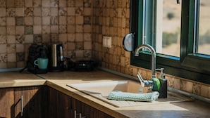 A kitchen with a sink, countertop, and wooden cabinets. - Pezoulia Cottages (Samothrace)