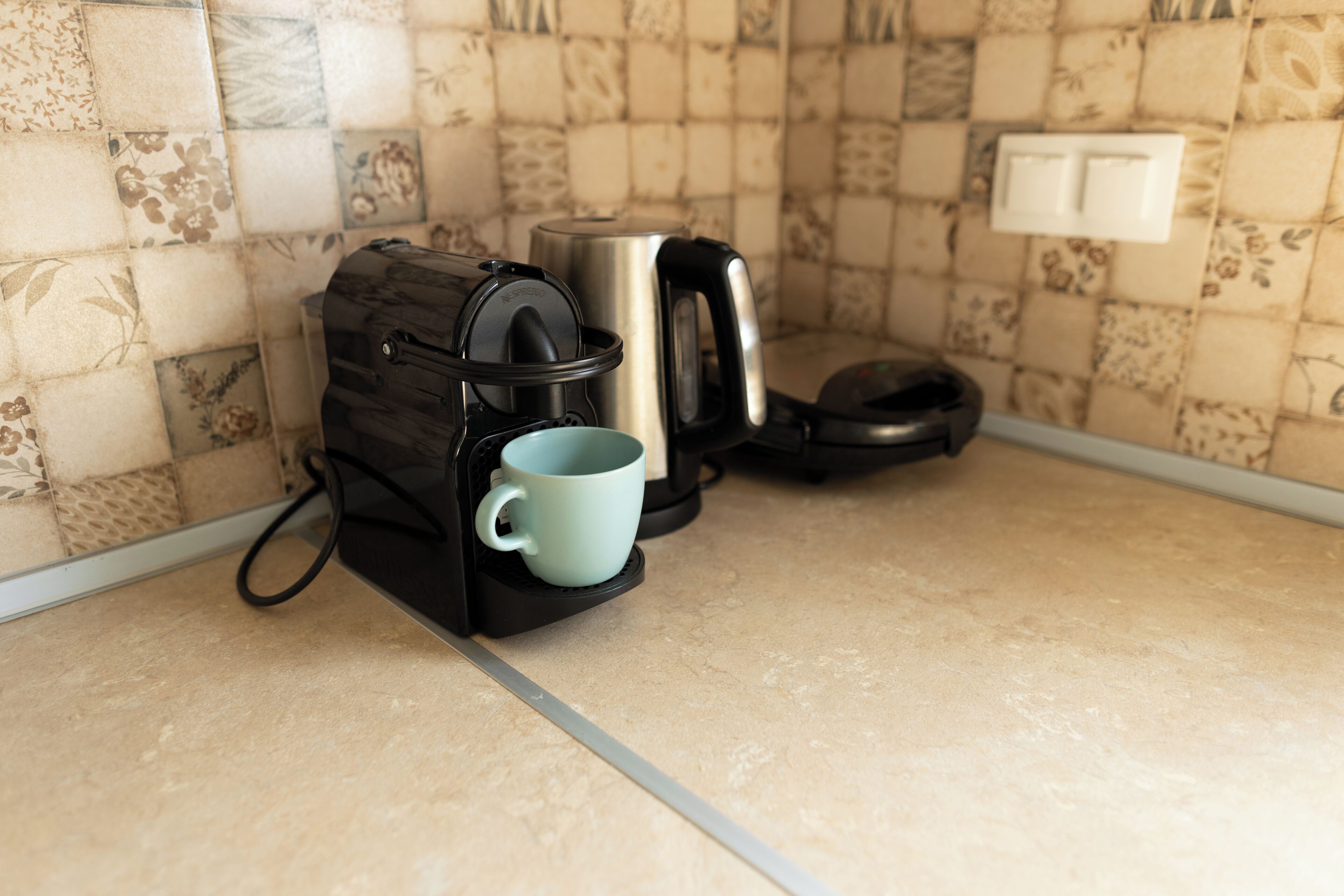 A kitchen with a coffee maker, a kettle, and a mug on the counter.