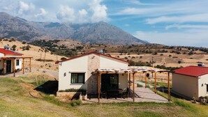 A residential area with a house featuring a patio with outdoor furniture, a small garden, and a view of mountains in the background. - Pezoulia Cottages (Samothrace)