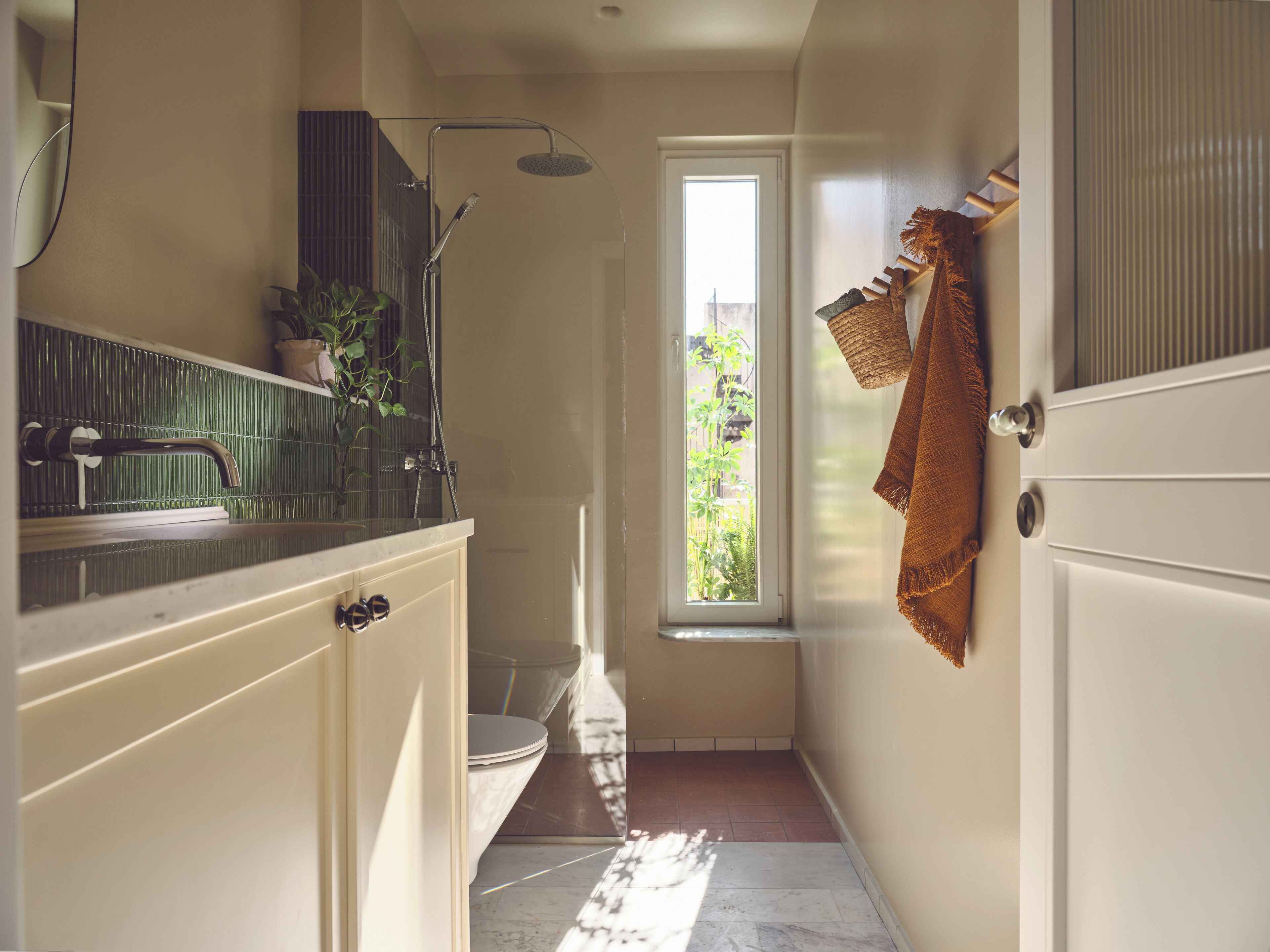 A narrow bathroom with a shower, a toilet, and a window.