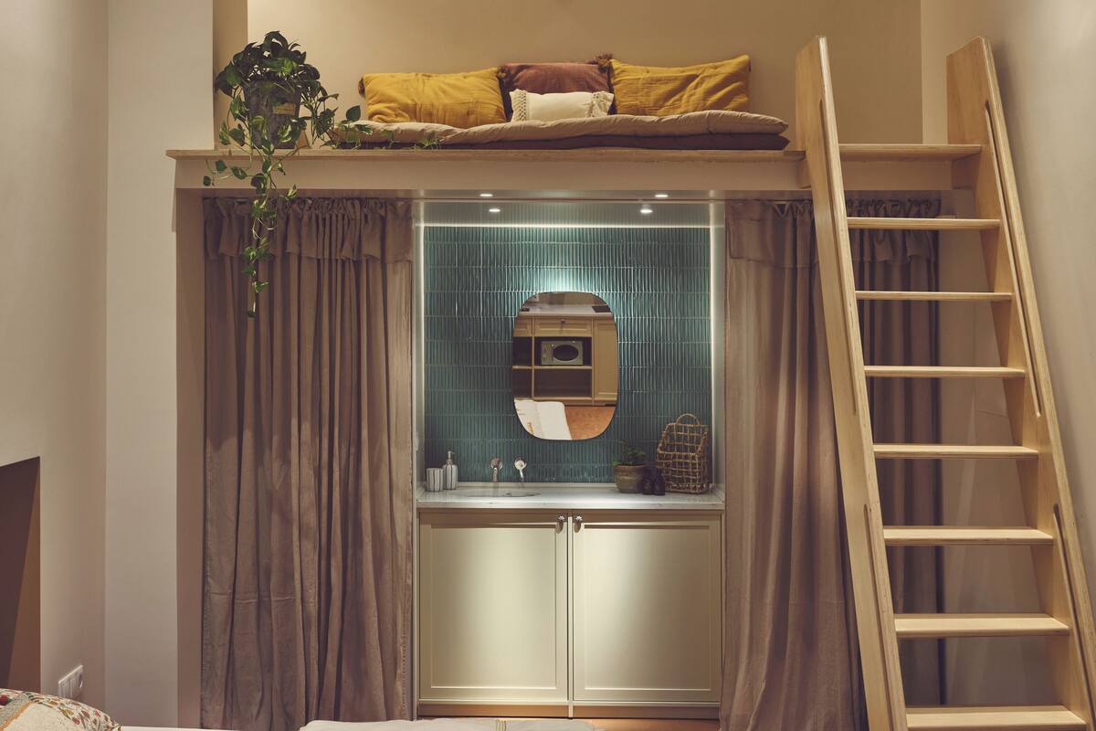 A bedroom with a bunk bed, a bedside table, a mirror, and a wooden ladder.