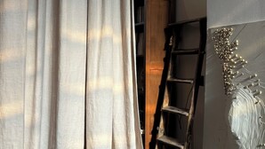 A room with a curtain, a ladder, and a wall with a decorative piece. - Melpomeni House (Athens)