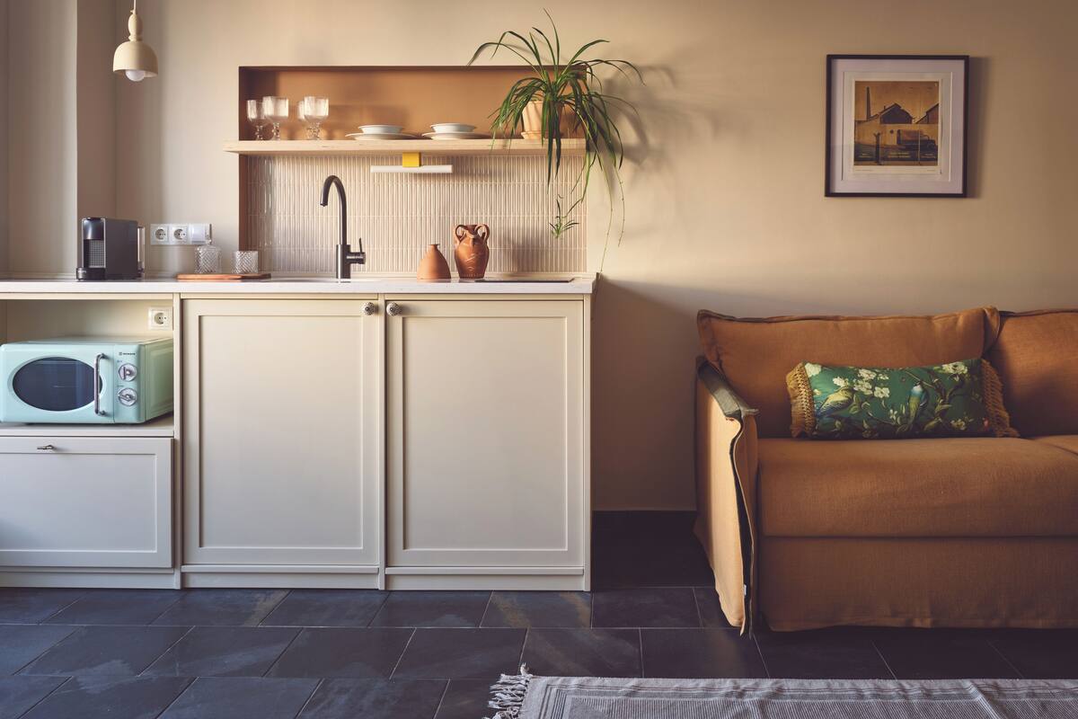 A modern kitchen with a built-in microwave, a sink, and a coffee maker. There is a plant on the counter and a framed picture on the wall.