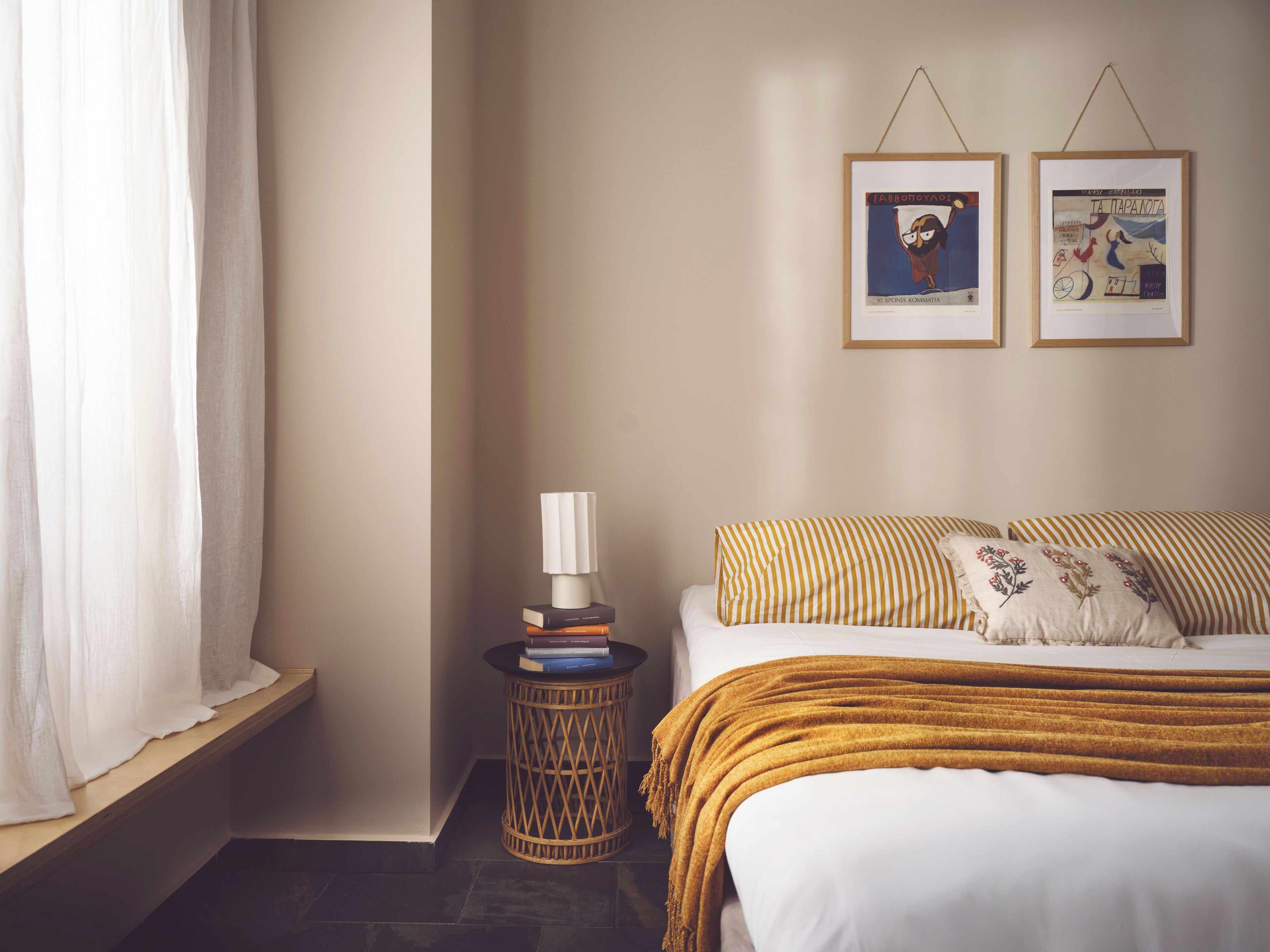 Un dormitorio con una cama, una mesita de noche con libros, una lámpara y dos cuadros en la pared.