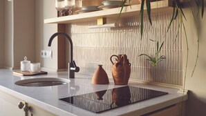 A modern kitchen with a black faucet, a built-in stove, and a white countertop. - Melpomeni House (Athens)