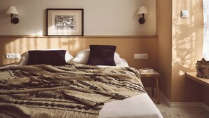 A hotel room with a bed, two wall-mounted lamps, a framed artwork, a nightstand, and a window with curtains. - Melpomeni House (Athens)