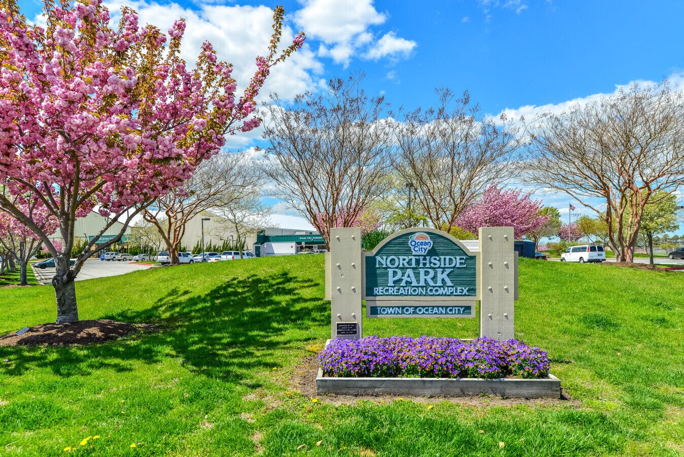 A sign for Northside Park Recreation Complex with a clear sky and blooming trees.