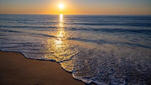 A beach at sunset with the sun reflecting on the water.