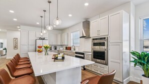 A modern kitchen with white cabinetry, a large island, stainless steel appliances, and pendant lighting.