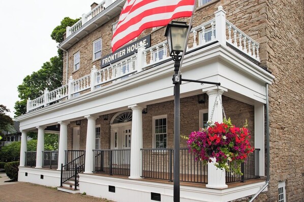 A two-story building with a porch, a sign reading "FRONTIER HOUSE," and a hanging flower basket.