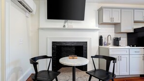 A modern kitchen with white cabinetry, a black tiled backsplash, a flat-screen TV mounted above the fireplace, and two black chairs around a marble table. - The McKinley (Lewiston)