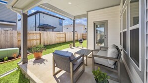 Eine überdachte Terrasse mit Gartenmöbeln, einem Grill und Blick auf angrenzende Häuser.