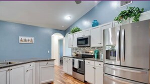 A modern kitchen with white cabinets, stainless steel appliances, and a wooden floor. - Your Sunny Escape - Private, screen lanai with heated pool. (Cape Coral)