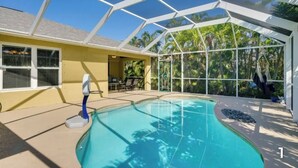 A covered swimming pool with a glass ceiling, surrounded by a yellow building and palm trees. - Your Sunny Escape - Private, screen lanai with heated pool. (Cape Coral)