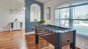 A modern room with a foosball table, a white cabinet, a mirror, and a large window. - Your Sunny Escape - Private, screen lanai with heated pool. (Cape Coral)