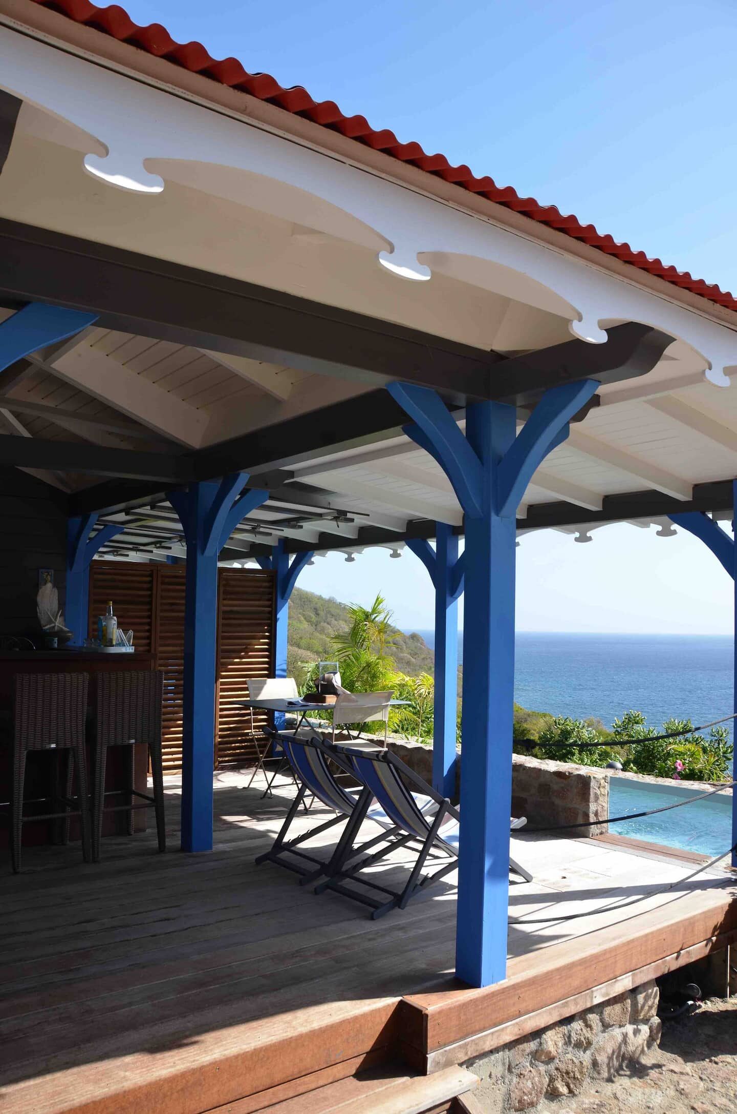A covered outdoor area with a pool, blue structural supports, and a view of the ocean.