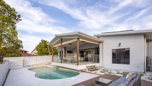 Een modern huis met een zwembad, terrasmeubels buiten en een overdekte patio.