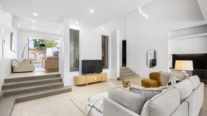 Een moderne woonkamer met een bank, een tv op een houten dressoir, en een trap naar een andere kamer.