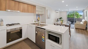 A modern kitchen with white cabinetry, a built-in oven, a dishwasher, and a microwave. There is a dining area with a table and chairs, and a sofa.