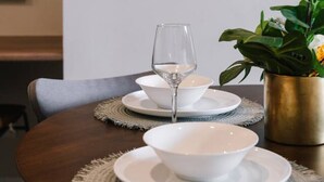 A dining table set with white plates, a glass, and a gold-colored vase with a plant.