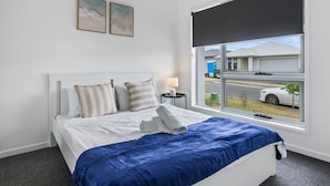 A hotel room with a bed, a window with a view of the street, and two framed pictures on the wall. - Brand New! Convenient Family Home w/ Workspace (Park Ridge)