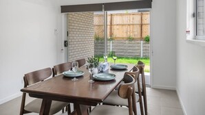 A dining area with a wooden table set for four, chairs, and a view of a backyard through a sliding glass door. - Brand New! Convenient Family Home w/ Workspace (Park Ridge)
