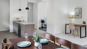 A modern kitchen with a central island, a dining area with a wooden table and chairs, and a small workspace with a desk and chair. - Brand New! Convenient Family Home w/ Workspace (Park Ridge)