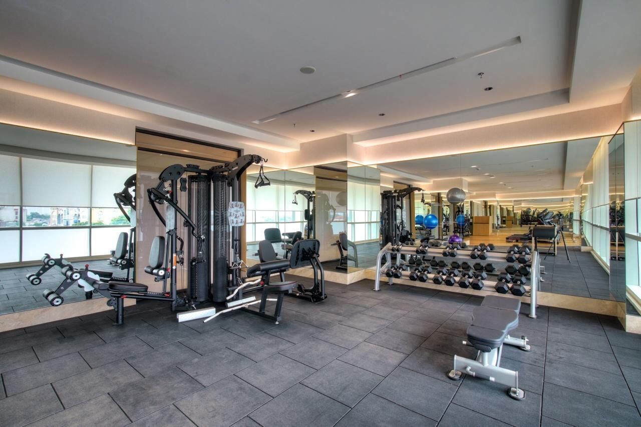A modern gym with various exercise equipment, mirrors, and a large mirror wall.