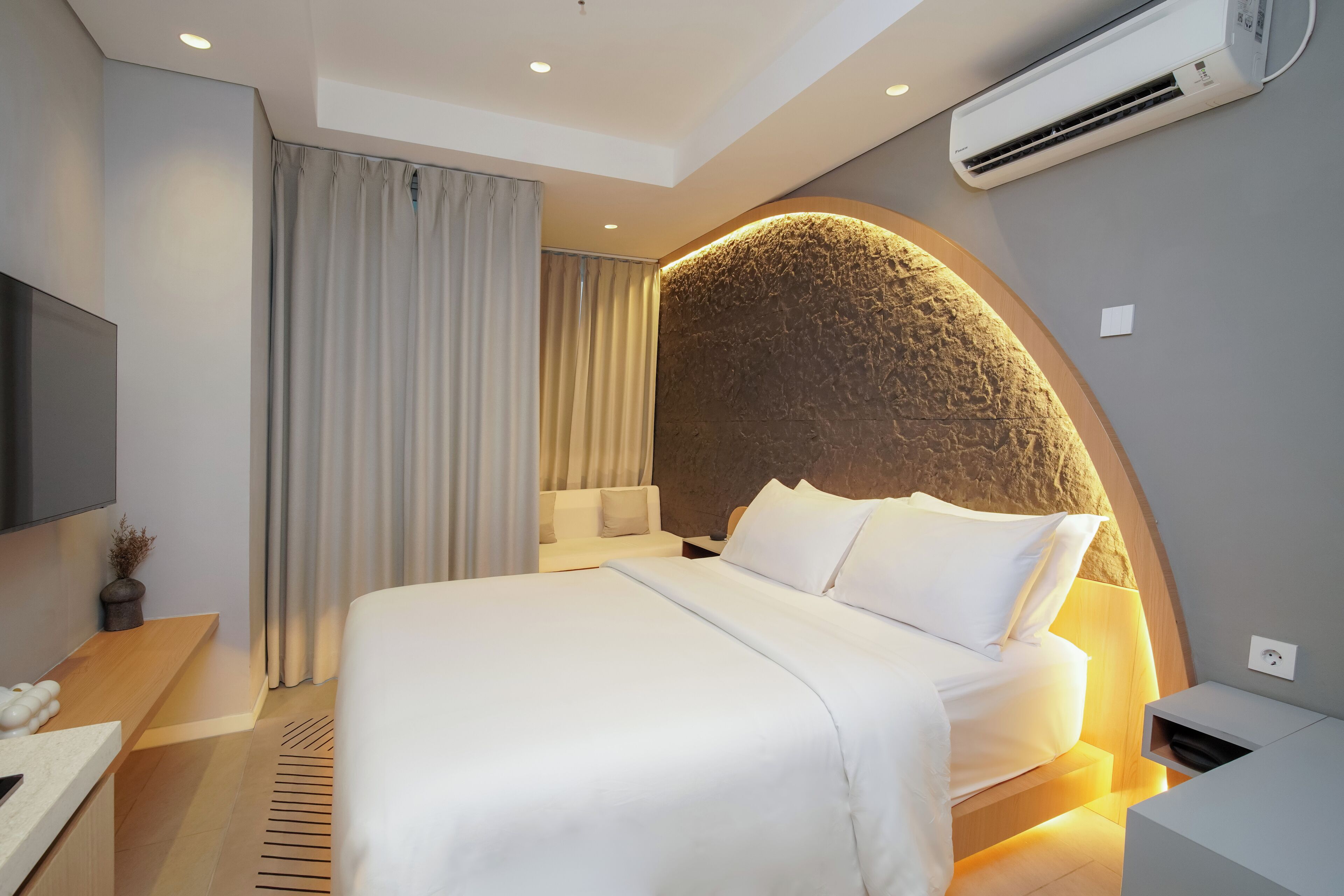Ein modernes Hotelzimmer mit einem großen Bett, einem Flachbildfernseher, einem Schreibtisch und einer Wandklimaanlage.
