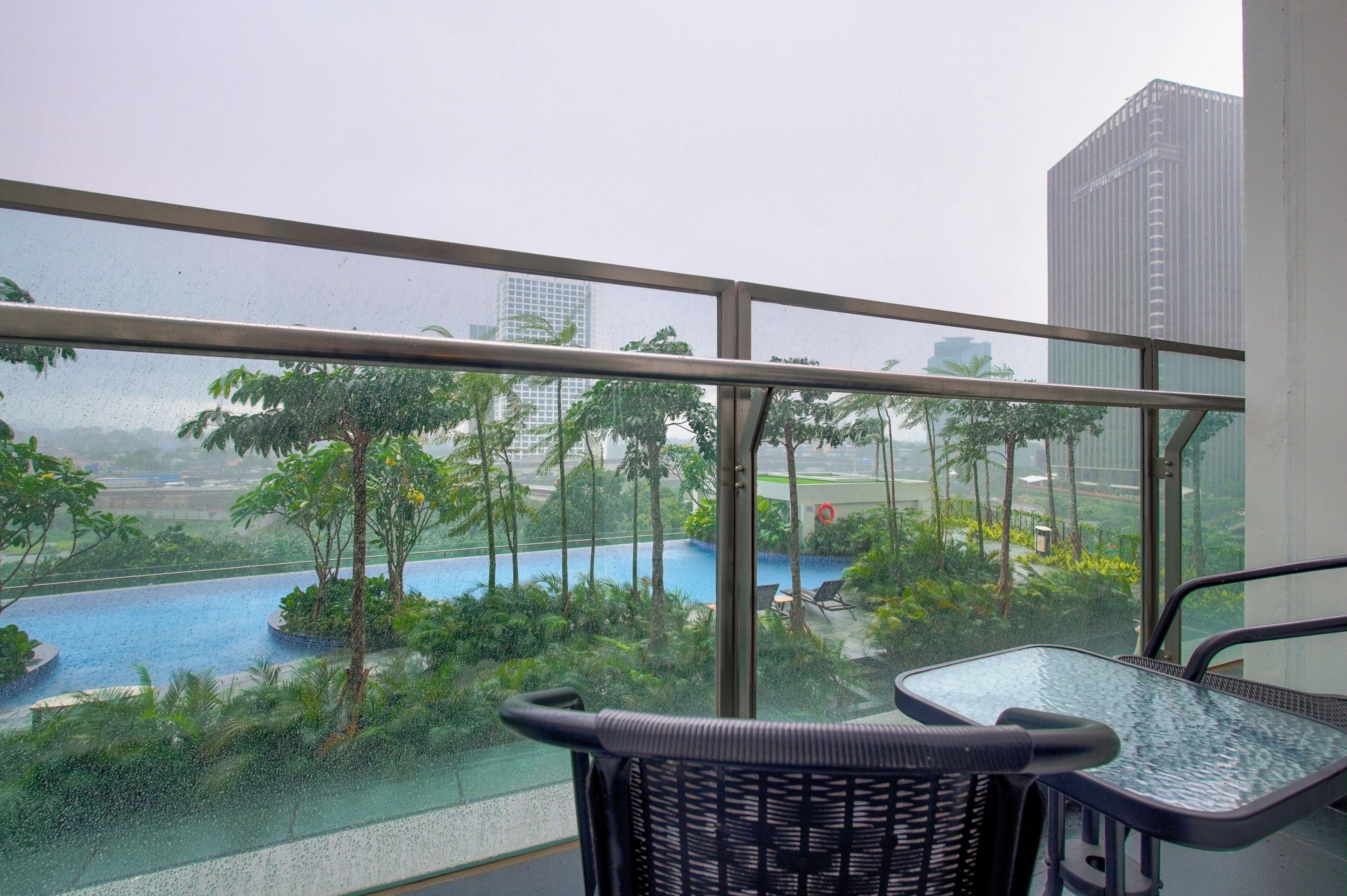 A balcony with a view of a swimming pool surrounded by greenery and tall buildings in the background.