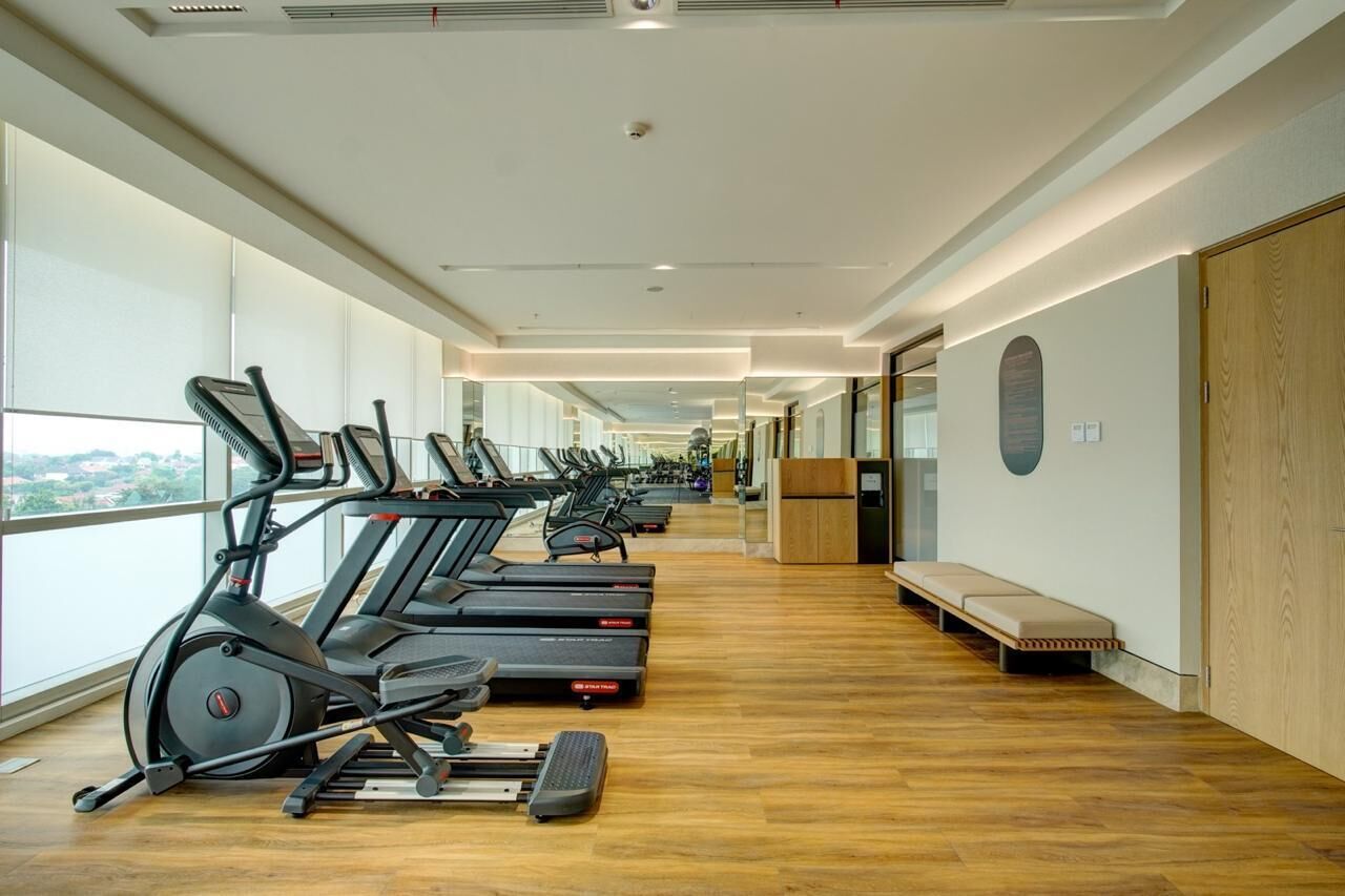 Un gimnasio con cintas de correr y equipo de ejercicio, amplias ventanas y piso de madera.