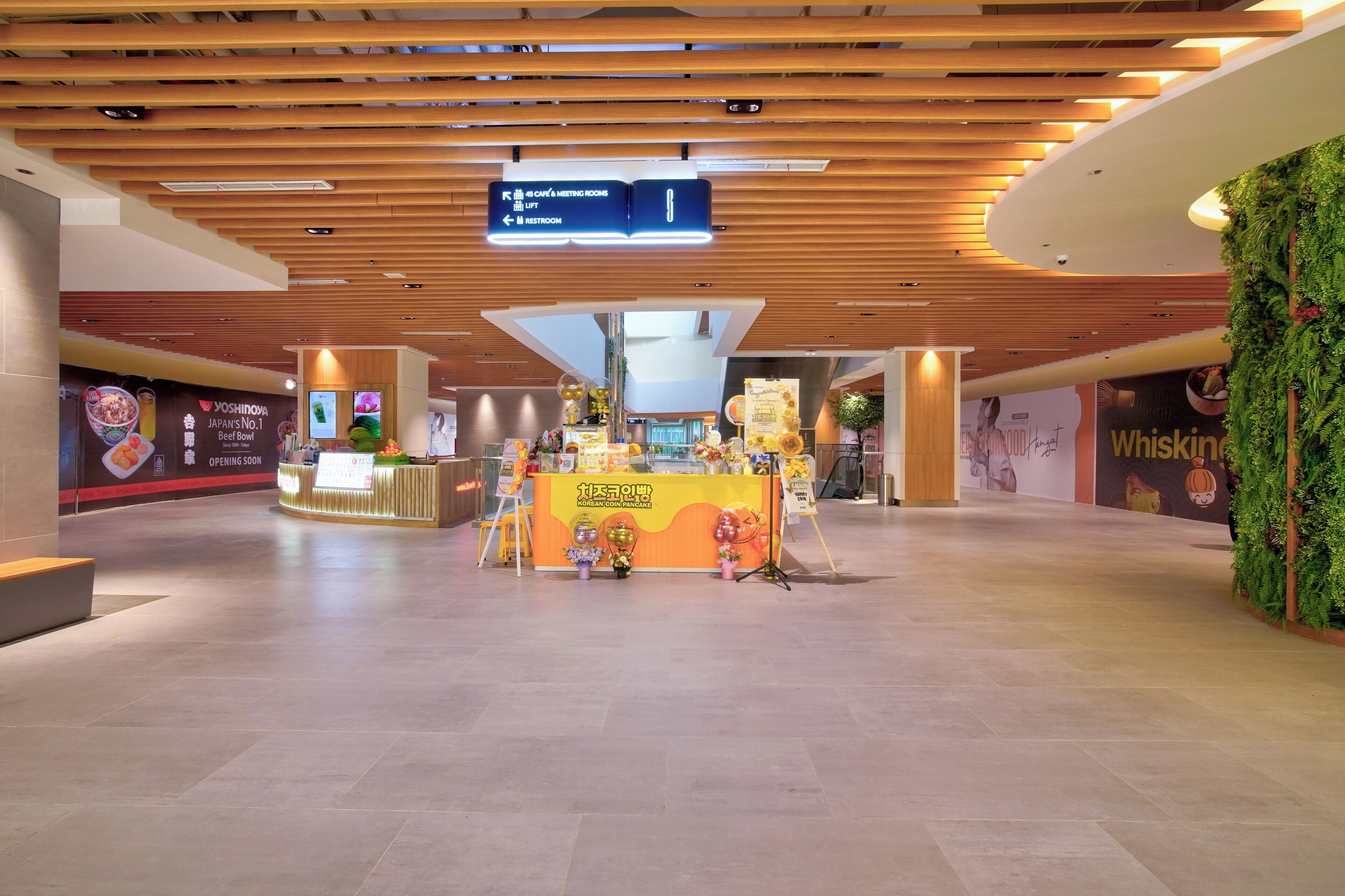 A modern interior with a wooden ceiling, a counter with a sign for Korean coin pancakes, and a digital sign above indicating directions.