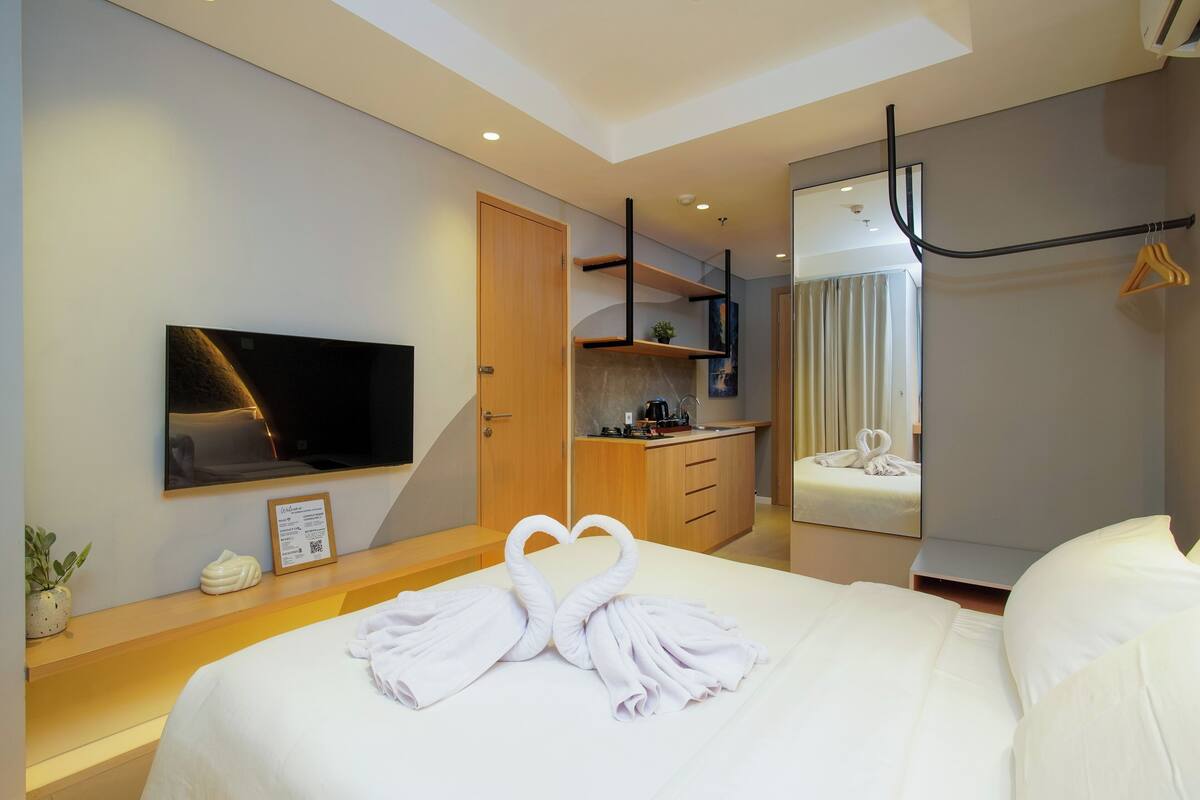 A hotel room with a bed, a TV, a desk, a mirror, and a wardrobe.