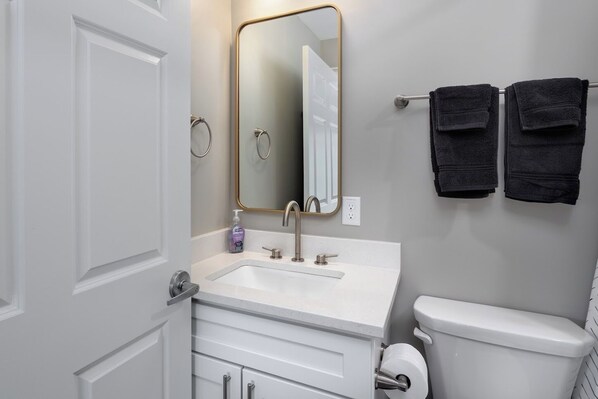 Een badkamer met een wit wastafelmeubel, een spiegel, een toilet en twee handdoeken aan een rek.