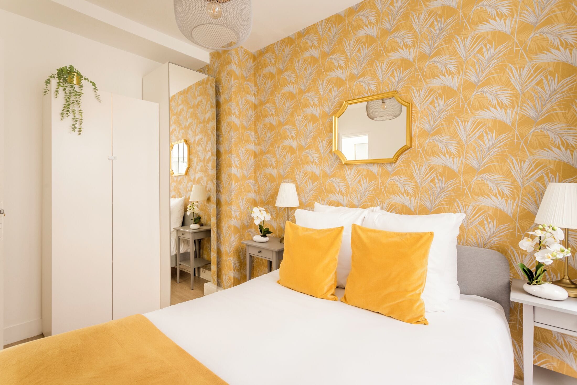 Ein Hotelzimmer mit Bett, Spiegel, Nachttisch mit Lampe und Schreibtisch mit Stuhl.