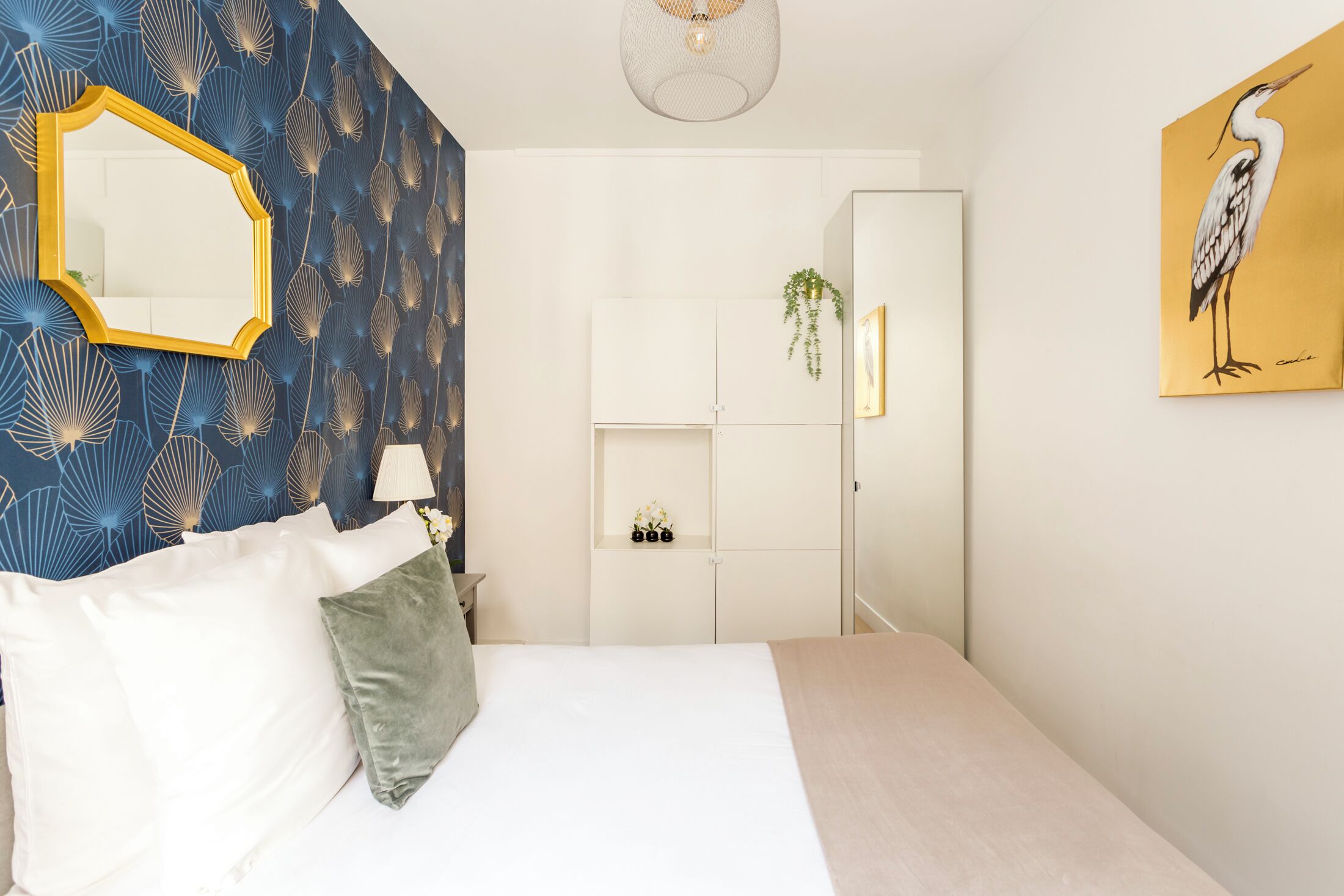 A bedroom with a bed, a mirror, a wardrobe, and a painting on the wall.
