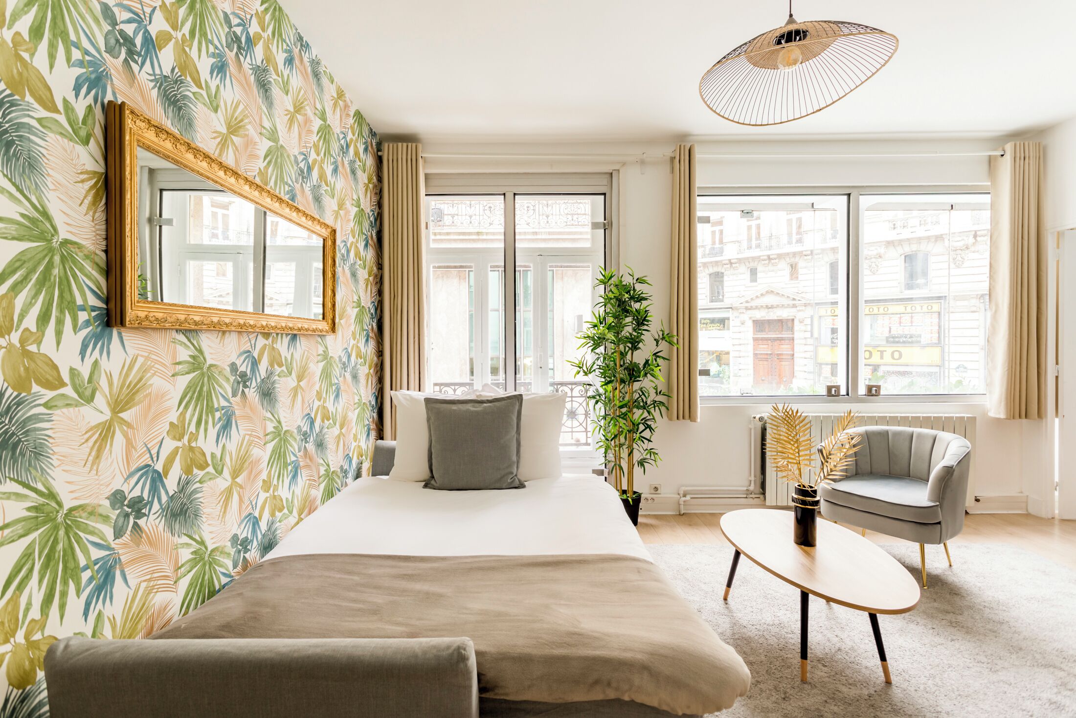 A bedroom with a bed, a bedside table, a chair, a large window, and a mirror on the wall.