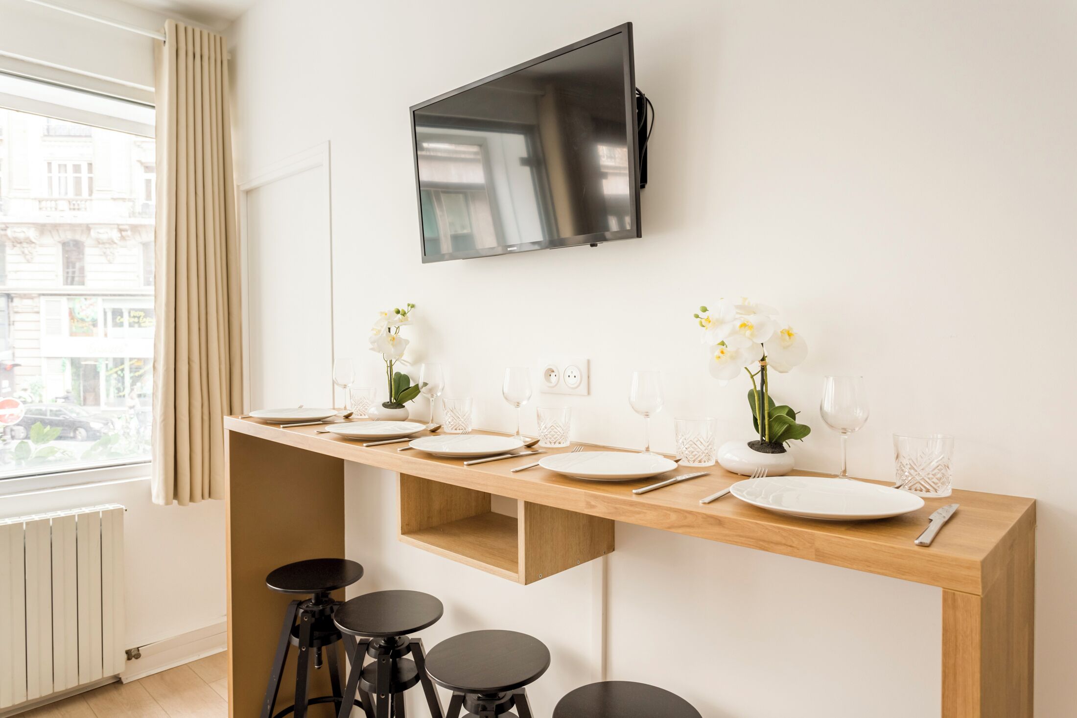 A modern kitchen with a wooden countertop, a TV mounted above, and a window with curtains.