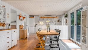 A spacious kitchen with white cabinetry, a wooden dining table, and a large window providing a view of the outdoors.