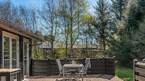 A wooden deck with a table and chairs, surrounded by a wooden fence and trees.