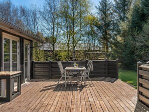 Una terraza de madera con una mesa y sillas, rodeada por una cerca de madera y árboles.