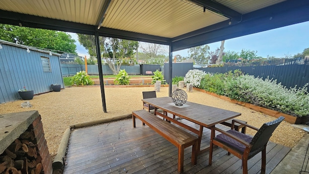 Un patio extérieur couvert, avec une table et des chaises en bois, un vase décoratif et un espace aménagé avec un foyer.