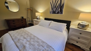 Un lit bien fait, avec du linge de lit blanc, une lampe de chevet, une commode avec un miroir et un tableau accroché au mur.
